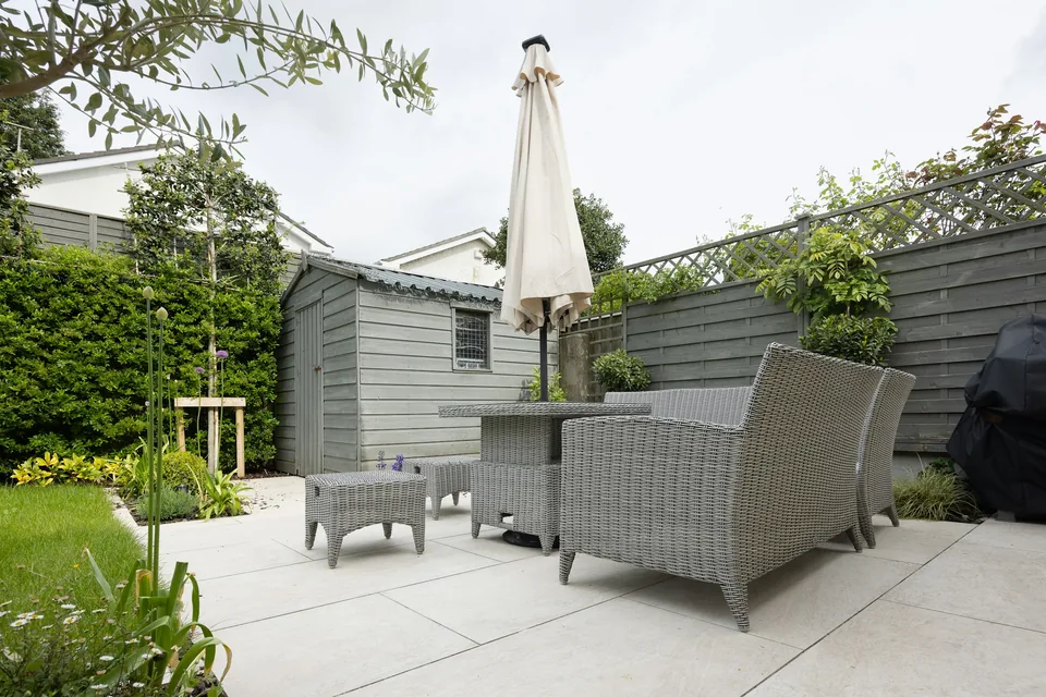 Kleiner Gartensitzplatz mit hellen Terrassenplatten, Pflanzbeet und grauem Holzsichtschutz.