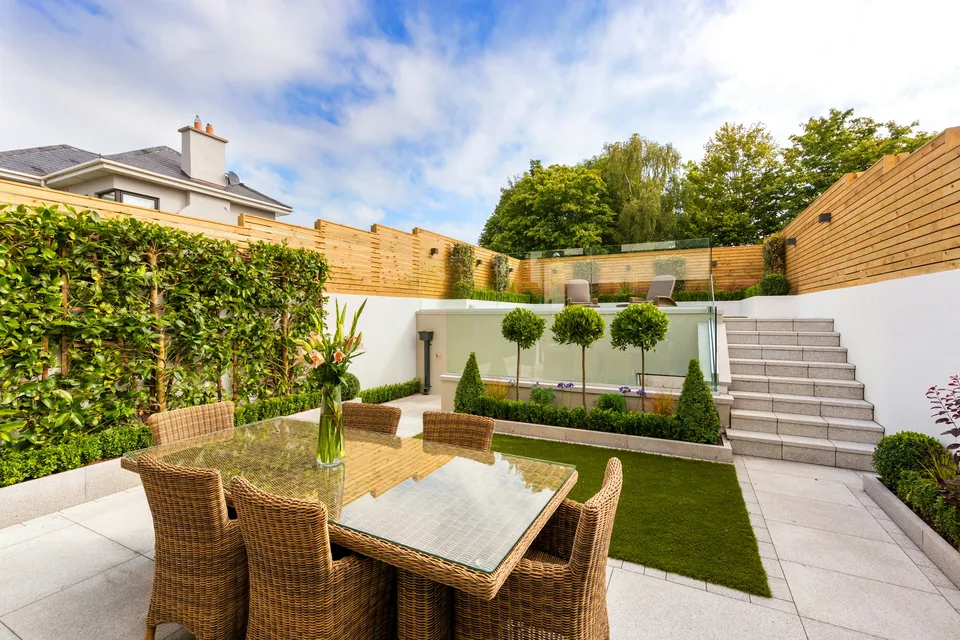 Gestalteter Privatgarten mit Pflanzflächen, heller Terrasse, Treppe und Holzsichtschutz.