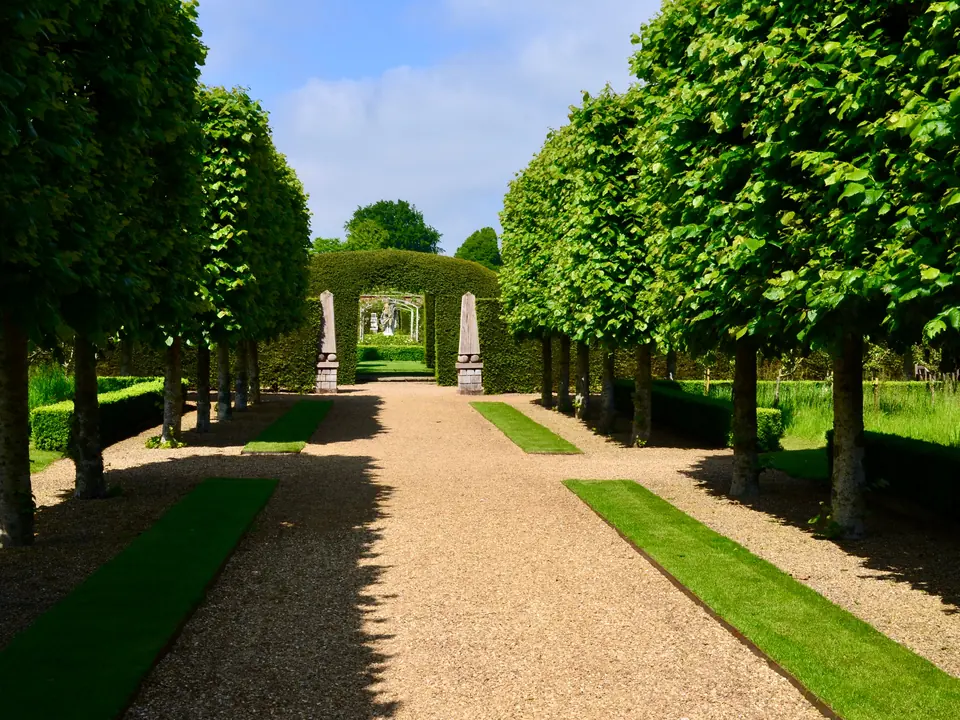 Symmetrischer Gartenweg zwischen geschnittenen Gehölzen.